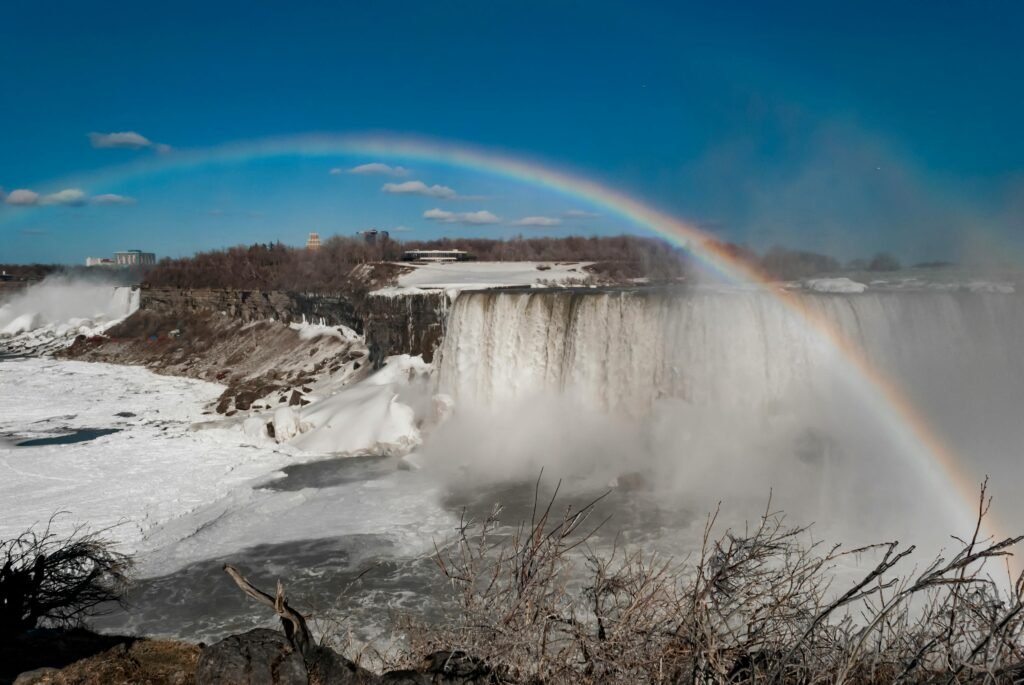 A stunning winter scene at Niagara Falls with a vibrant rainbow, captured in vivid daylight.