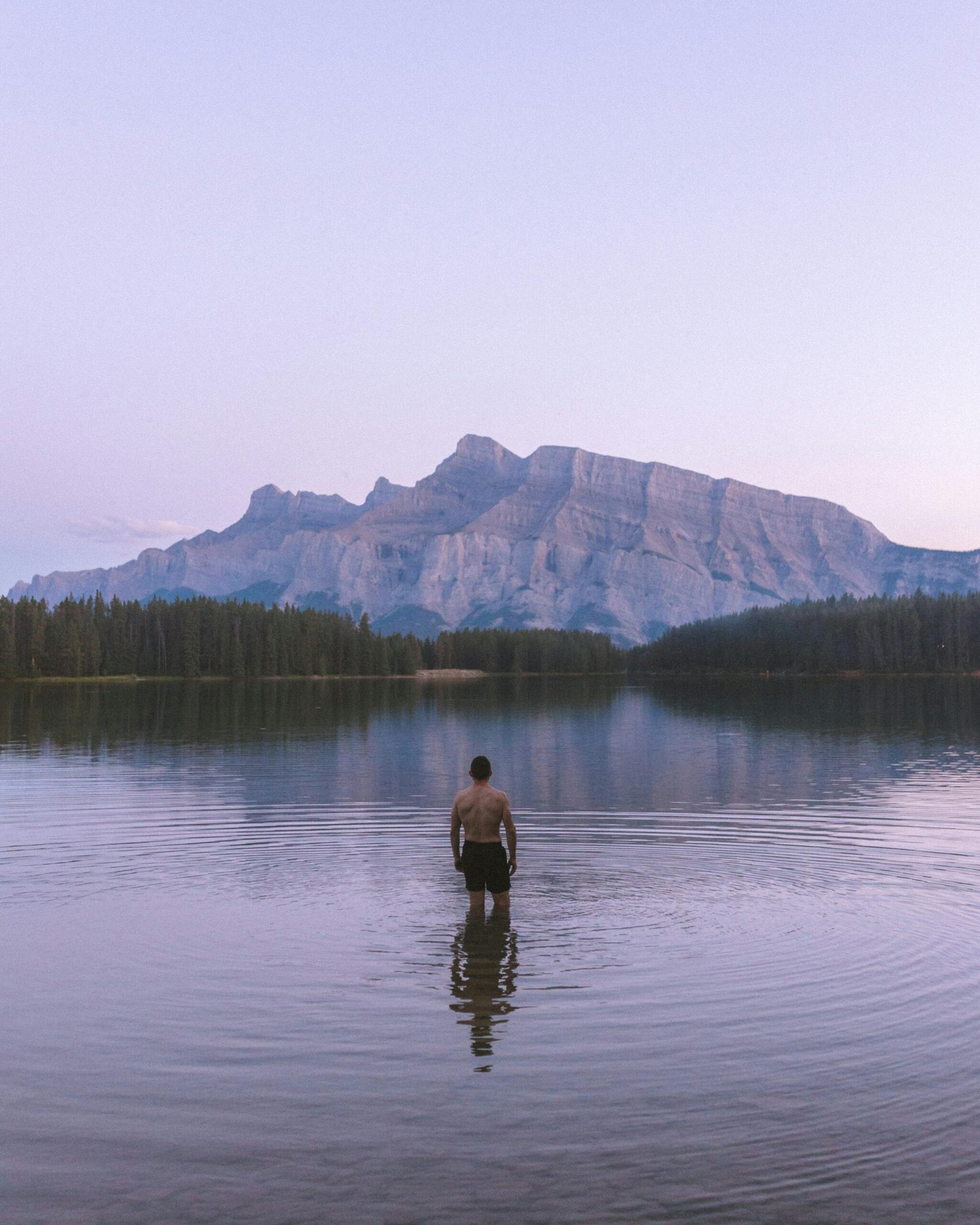 A lone man stands in tranquil Two Jack Lake with a stunning mountain backdrop in Alberta, Canada.