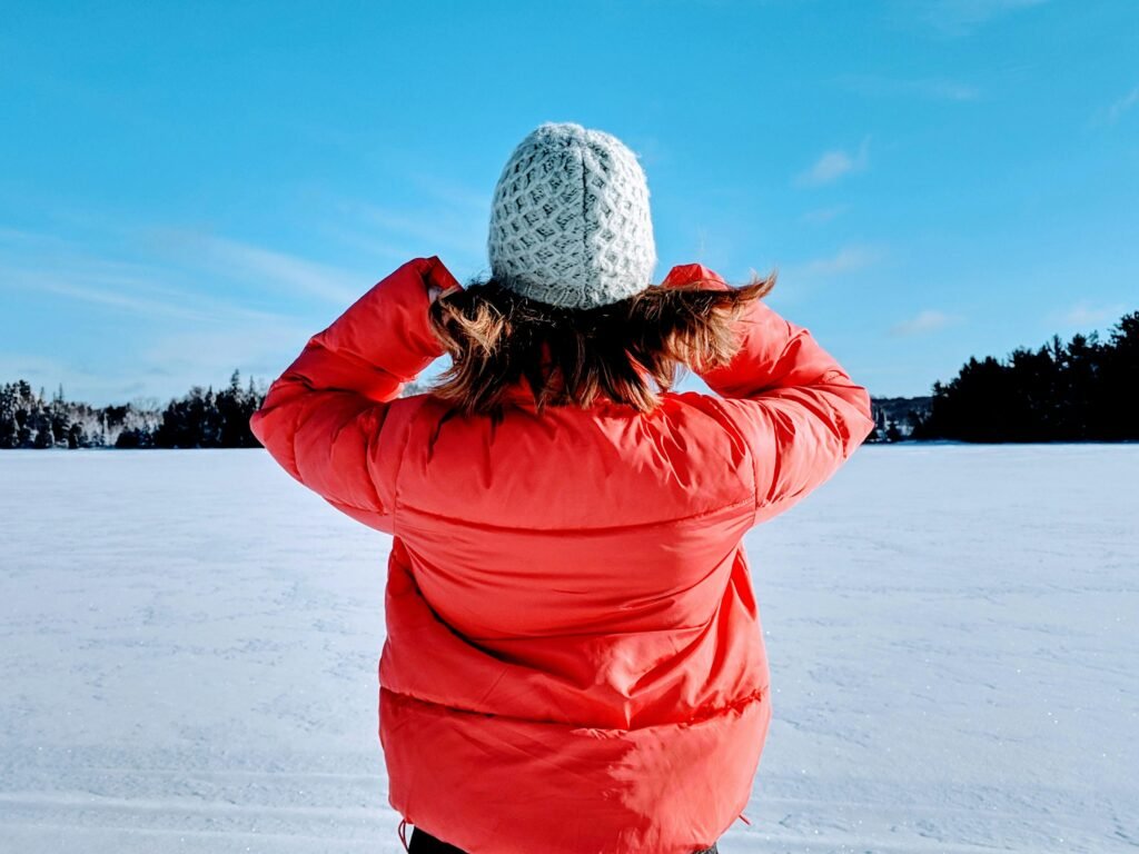 A person in a red jacket and beanie enjoys a crisp winter day in Whitestone, Canada.