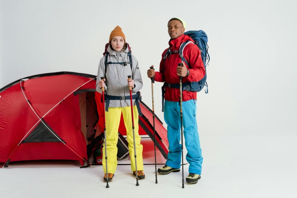 Two hikers in colorful gear pose with trekking poles and a red tent in a studio.