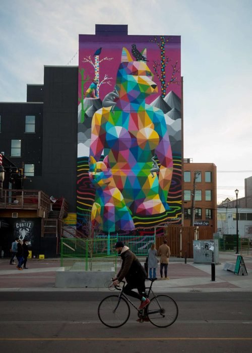 A guy is riding a bicycle and there is a mural behind him. Its at Whyte Avenue, Edmonton