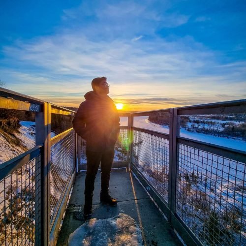 A guy is posing in Keillor point in Edmonton at the afternoon. There is a sunset behind the guy.